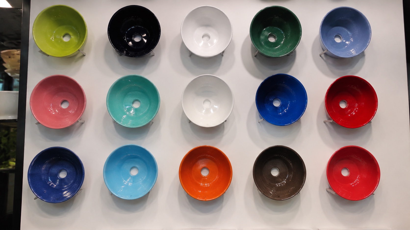 Colourful round ceramic art basins in many glaze colours on a showroom display wall