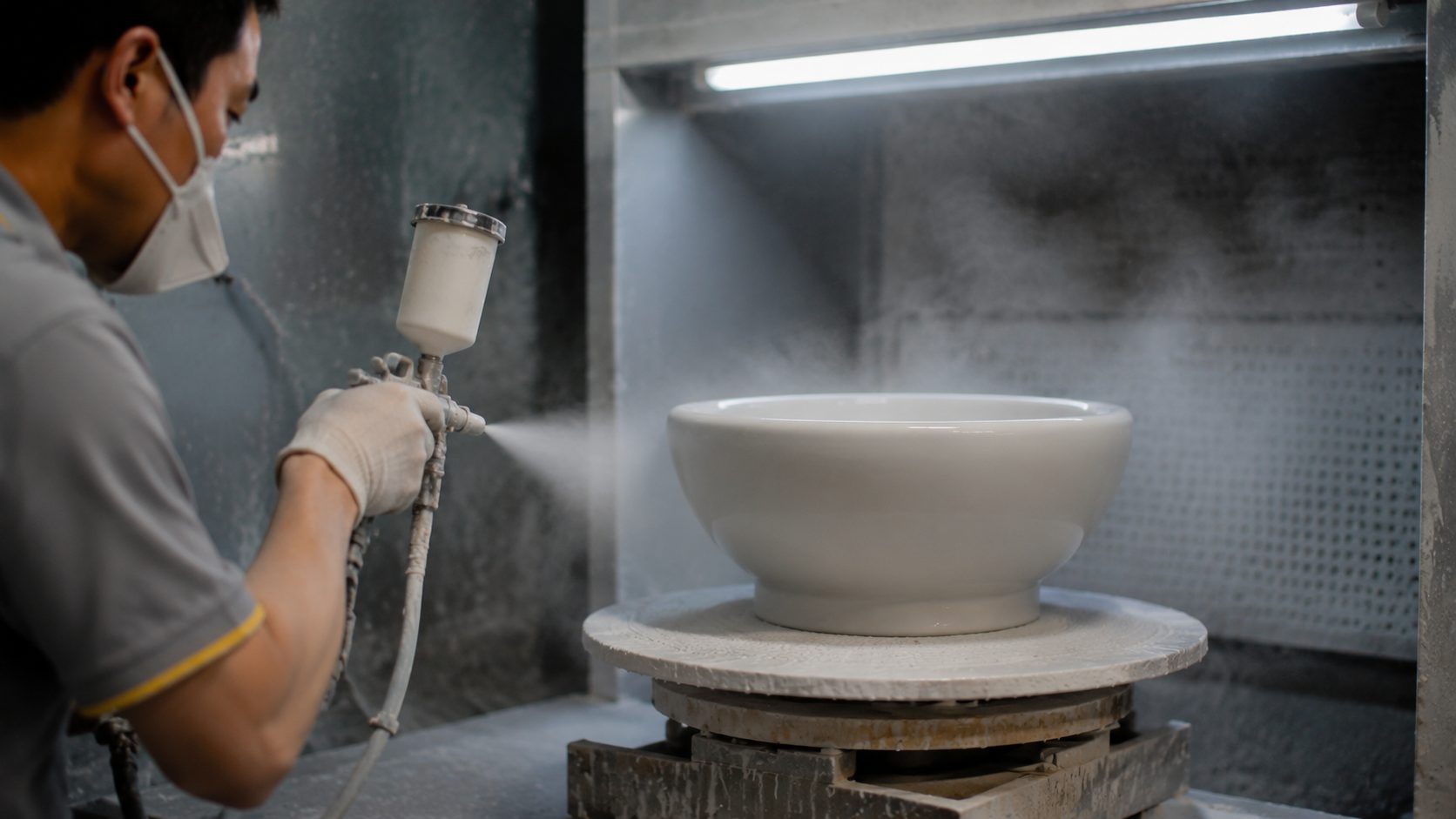 Kiln cars loaded with white ceramic bodies queued at a tunnel kiln mouth with a warm glow inside, part of the firing stage of the production timeline