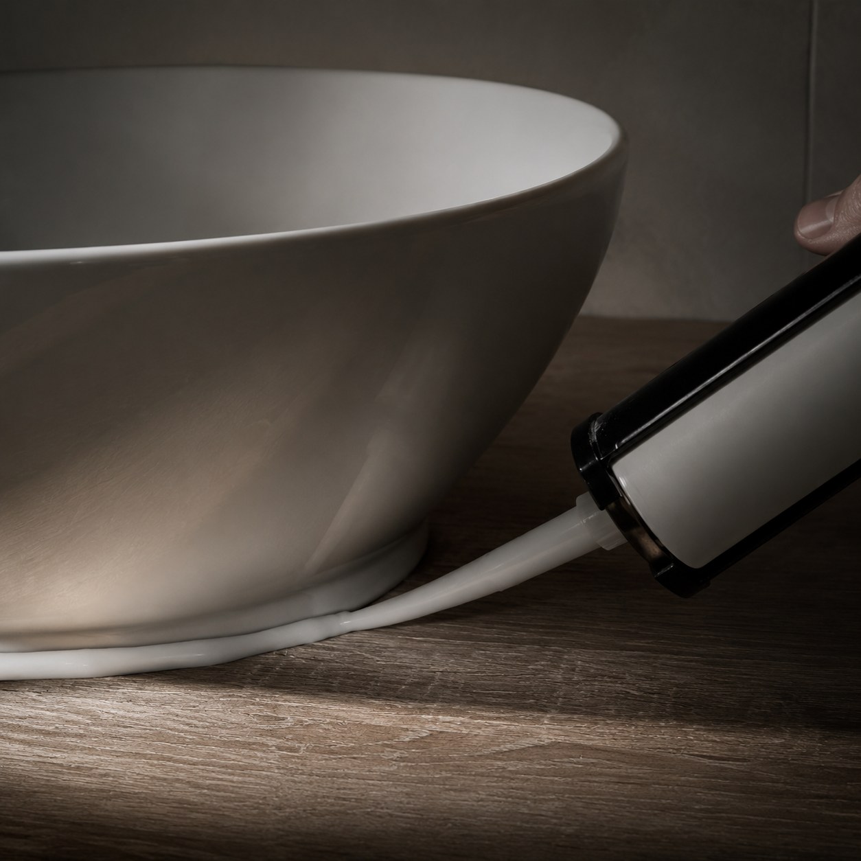 Close-up of a ceramic countertop basin sitting on a counter showing the drain hole, waste and silicone base seal