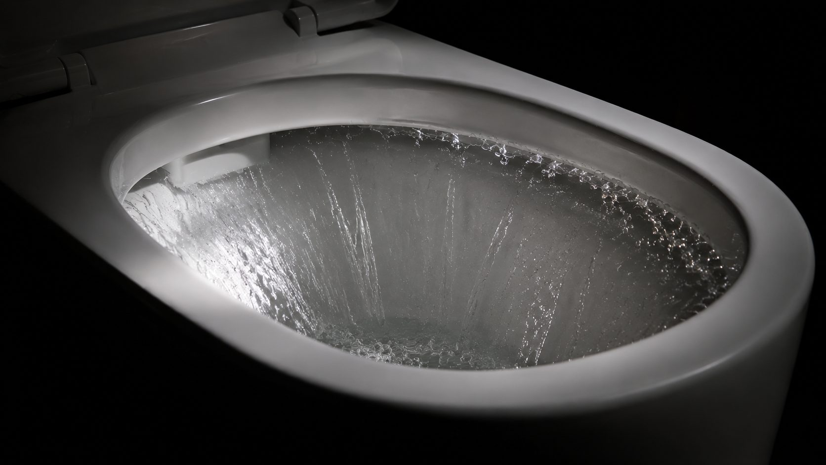 Clear water sweeping in one continuous sheet around a clean white rimless ceramic toilet bowl during a flush
