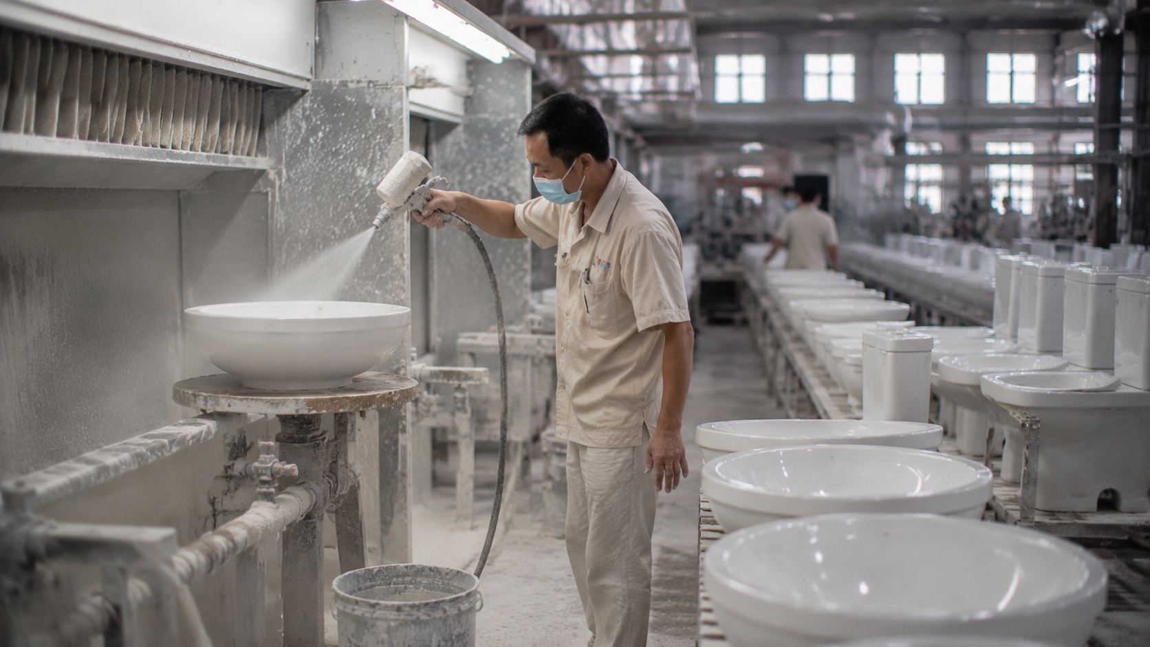 Spray-glazing a white ceramic wash basin at a ceramic sanitaryware factory in Chaozhou, China